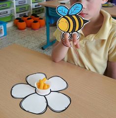 a young boy sitting at a table with a paper flower and bee cutout in front of him