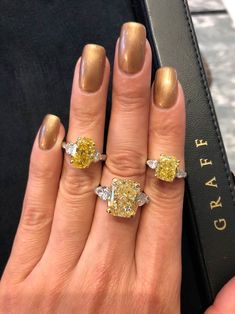 a woman's hand with two yellow and white diamond rings on top of it