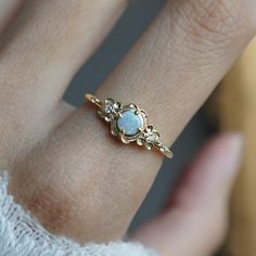 a woman's hand wearing a gold ring with an opal stone in the center