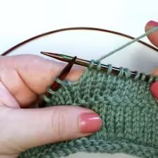 two hands are holding yarn and crocheting together