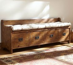 a wooden bench sitting on top of a rug in a living room next to a window