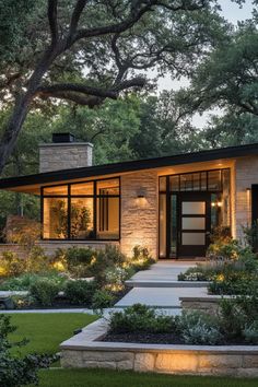 a modern house is lit up at night in the yard with trees and bushes surrounding it