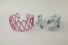 two metal bracelets sitting next to each other on a white surface with blue and green beads