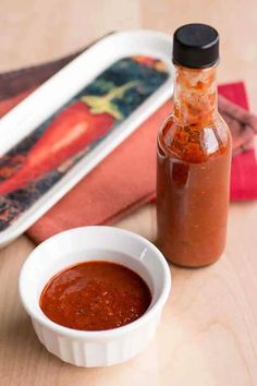 a small white bowl filled with sauce next to a bottle of hot sauce on a wooden table