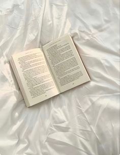 an open book laying on top of a white sheeted bed with the cover pulled down