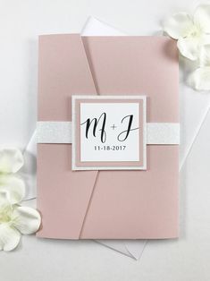 a pink wedding card with white flowers on the side and a monogrammed envelope