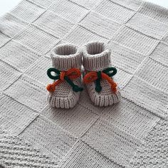 a pair of knitted baby booties sitting on top of a white blanket with orange and green bows