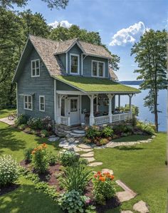 a house that is by the water with flowers in front of it and some trees