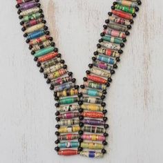 a necklace made out of rolled up newspaper beads on a white wooden background with space for the letter y