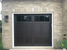 a black garage door in front of a brick building with two planters next to it