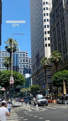 people crossing the street in front of tall buildings and palm trees on a sunny day