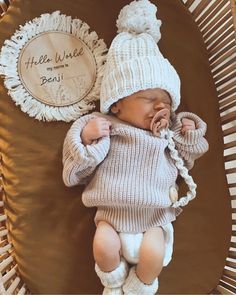 a baby sleeping in a basket wearing a hat