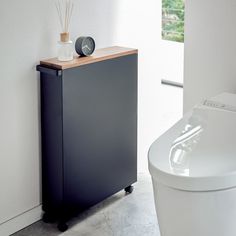 a white toilet sitting next to a black cabinet in a bathroom with a wooden top