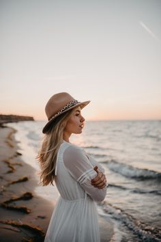 a woman standing on top of a beach next to the ocean in a white dress