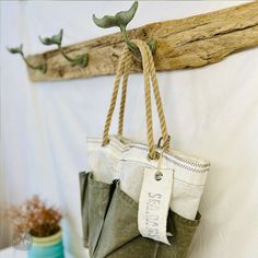 an origami bag hanging from a wooden branch on a white wall next to a potted plant