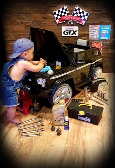 a small child standing next to a car with tools in front of it on top of a wooden table