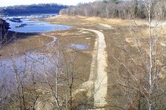 a dirt road in the middle of a field next to some water and trees with no leaves on them