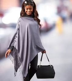 a woman walking down the street carrying a black purse and wearing a gray poncho