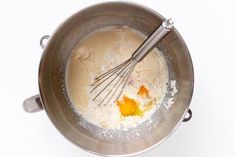 a metal bowl filled with batter and eggs on top of a white table next to a whisk