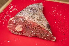 a piece of meat sitting on top of a red cutting board with seasoning sprinkles