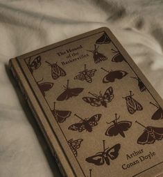 an old book with butterflies on it sitting on a white bed sheet in front of a blanket