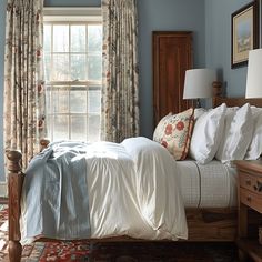 a bed sitting in a bedroom next to a window covered in white sheets and pillows