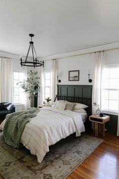 a bedroom with a bed, chair and rug on the hardwood floored floor in front of two windows