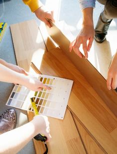 three people standing around a wooden table with paint swatches on it and one person holding a tape