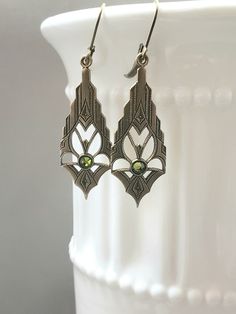 These modern Deco earrings are a great example of classic 1920s style. They feature ornate Art Deco style brass pendants. The pendants have a tiny olivine green crystal at the center These elegant earrings measure 2 inches long from the top of the ear wires to the bottom of the pendants. I love the simplicity of these Art Deco inspired earrings; perfect for everyday or evening. ABOUT THIS COLLECTION What are the three style essentials Jazz Age flappers like Clara Bow, Louise Brooks, and Zelda Fi Antique Finish Bronze Wedding Earrings, Elegant Brass Earrings With Antique Finish, Antique Bronze Earrings For Wedding, Victorian Wedding Earrings With Antique Finish, Antique Filigree Chandelier Earrings For Formal Occasions, Art Deco Pierced Jewelry For Anniversary, Vintage Dangle Chandelier Earrings For Anniversary, Vintage Chandelier Dangle Earrings For Anniversary, Elegant Brass Chandelier Earrings For Formal Occasions