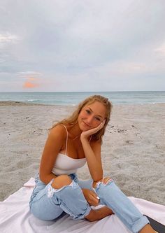 a beautiful young woman sitting on top of a white blanket