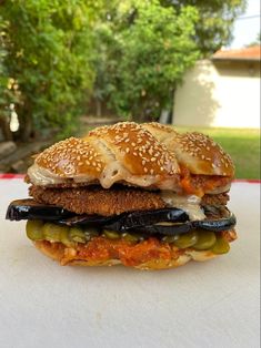 a sandwich with meat, cheese and pickles on it sitting on a table outside