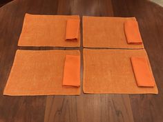 four pieces of orange cloth laid out on a wooden table with placemats and napkins