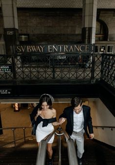 a man and woman walking down an escalator in a train station holding hands