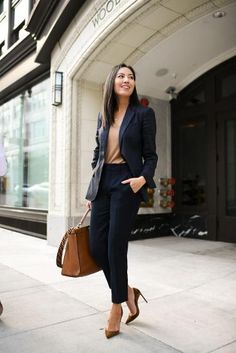 The business attire is composed of a navy blue blazer and navy blue trousers, creating a classic and professional look. A beige tee shirt complements the navy blue color of the blazer and trousers, adding a touch of softness to the outfit. To complete the outfit, a pair of camel brown heels and a matching handbag are added. Overall, this business attire exudes sophistication and professionalism while still being comfortable and stylish. Business Professional Outfits, Career Outfits, Lawyer Outfit, Professional Attire, Business Outfit, Mode Inspo, Work Outfits Women, Work Wardrobe