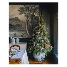 a decorated christmas tree sitting in front of a painting on the wall next to a dining room table