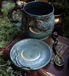 a blue cup and saucer sitting on top of an old book next to a spoon