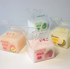 four glass containers with different types of milk and fruit labels on them, sitting next to each other