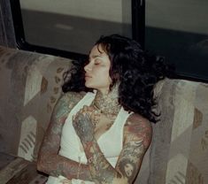 a woman with tattoos on her arms sitting on a couch next to a train window