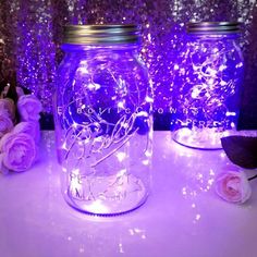 two mason jars with fairy lights in them sitting on a table next to some flowers