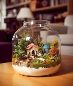 a glass jar filled with plants and a house in the middle on top of a wooden table