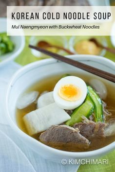 a bowl of soup with meat, vegetables and an egg in it on a table