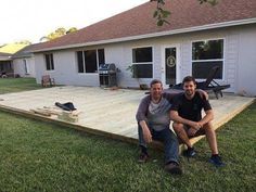 two men sitting on a wooden deck in front of a house