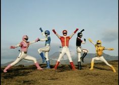 five people dressed in colorful costumes standing on top of a hill with their arms up