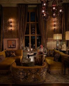 a man sitting on a couch in a living room with chandelier hanging from the ceiling