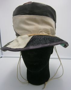 "Handmade leather patchwork asymmetric medium brimmed hat. The hat is constructed from mixed coloured patches of leather machine stitched, with a cord fastening which passed through brass eyelets. The hat features an asymmetric brim which varies in depth from about 6 cm / 2.5\" to about 8.5 cm / 3.5\". Rim circumference approximately 56 cm / 22″, edged in white cotton tape; height of crown is about 11 cm / 4.5″. Please measure to check the hat circumference and height size you need before ordering, or contact me with any queries. The tape measure pictured is in cm. The hat is constructed in off-cuts / up-cycled leather and is lined in green 100% cotton canvas fabric. Handmade leather label inside crown \"Handmade by Reynold Trim\", who is the Entertainer Trim Bling Star." Crown Handmade, The Entertainer, Crown Hat, Brimmed Hat, Cotton Canvas Fabric, Leather Patchwork, Leather Label, Slouchy Hat, Brim Hat