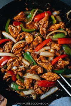 chicken and peppers stir frying in a skillet with chopsticks on the side