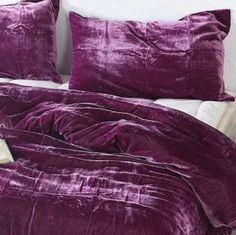 a bed with purple sheets and pillows on top of it in front of two paintings