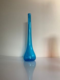 a blue glass vase sitting on top of a white table next to a light colored wall