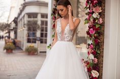 a woman in a white wedding dress standing on the sidewalk next to a flower covered archway