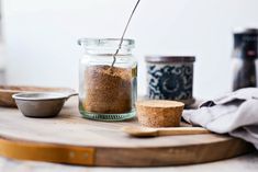 a jar filled with spices sitting on top of a wooden cutting board next to two spoons